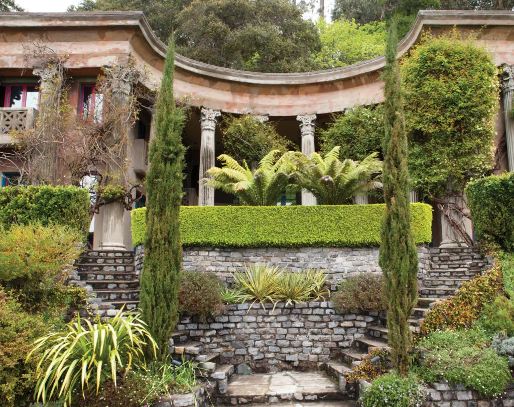 The Temple of Wings, viewed from the driveway, is open to the Western sun and views across beautifully wooded Berkeley hillsides. Bernard Maybeck is generally credited with the design (though he had a falling out with his client, Florence Treadwell Boynton, and the young architect Randolph Monro supervised the construction in 1914). A pair of sheltering wings surmount a peristyle of 34 Corinthian columns, cast in concrete in place. Originally open to the elements, it was rebuilt after a 1924 wildfire and the enclosed wings were added, along with a miniscule kitchen excavated into the hillside. Paint colors are authentic to this period. (Photography by Lisa Romerein)
