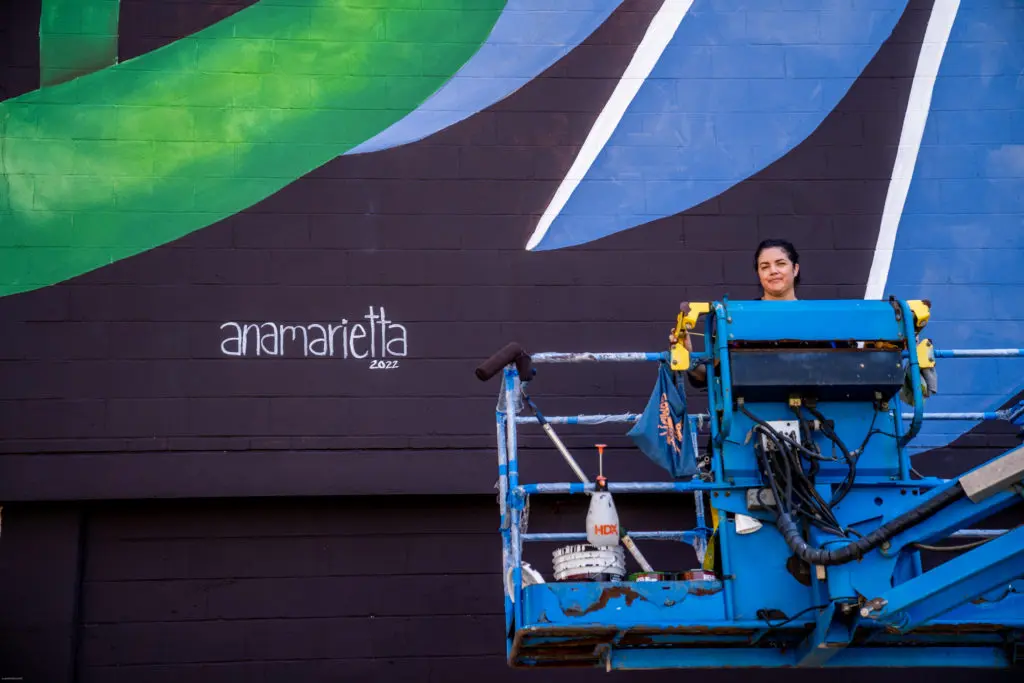 Ana Marietta stands next to her signature on "Sharing the World." (Photo by @superkant and @cyvisuals_, courtesy Street Art for Mankind)
