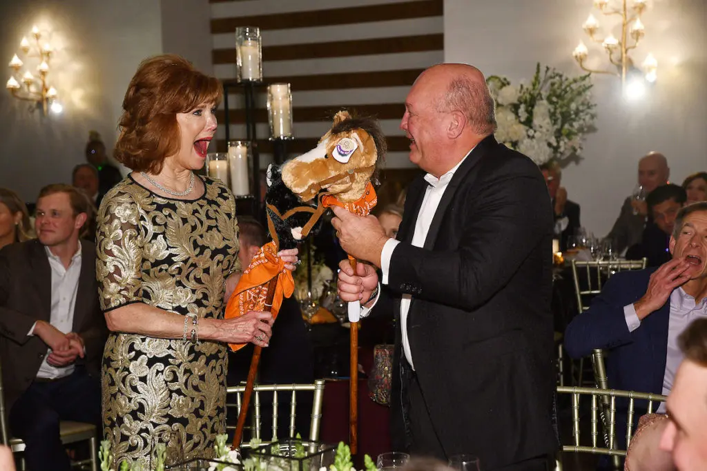 Honorees Martha & Buzz White are surprised with two stick horses representing the donation of two real horses in their honor at the Camp for All gala, held at The Revaire.