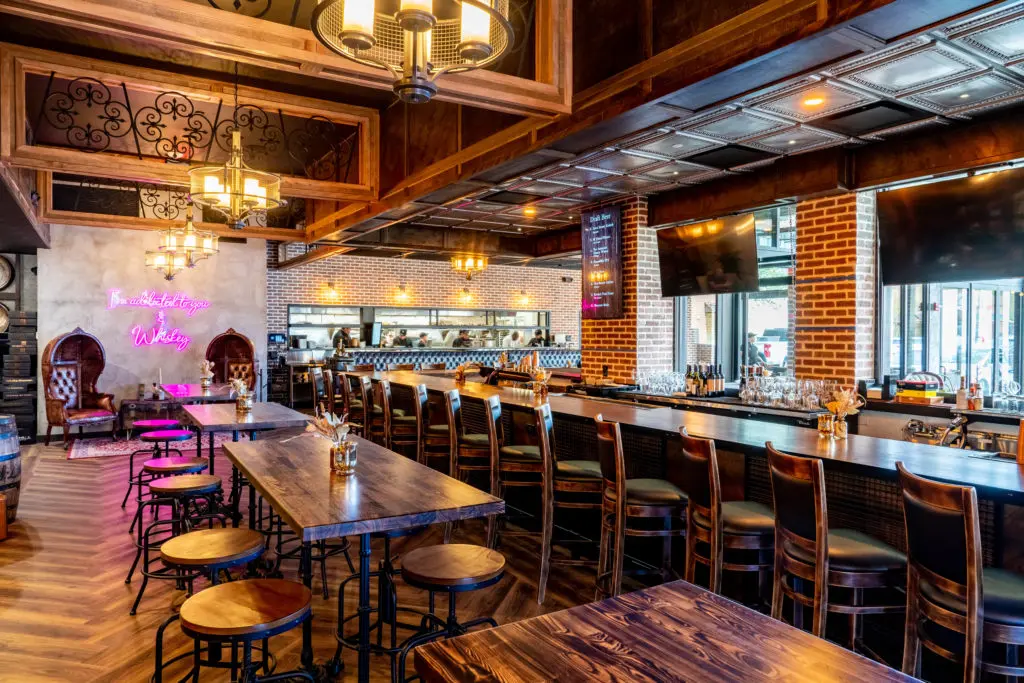 Inside the new Bosscat, the 5,000 square foot space with seating for 130 guests plays off the trend of industrial, rustic aesthetics–read: exposed brick, reclaimed wood, dark leather banquettes, and massive whiskey barrels all over the place. (Photo by Dylan McEwan)