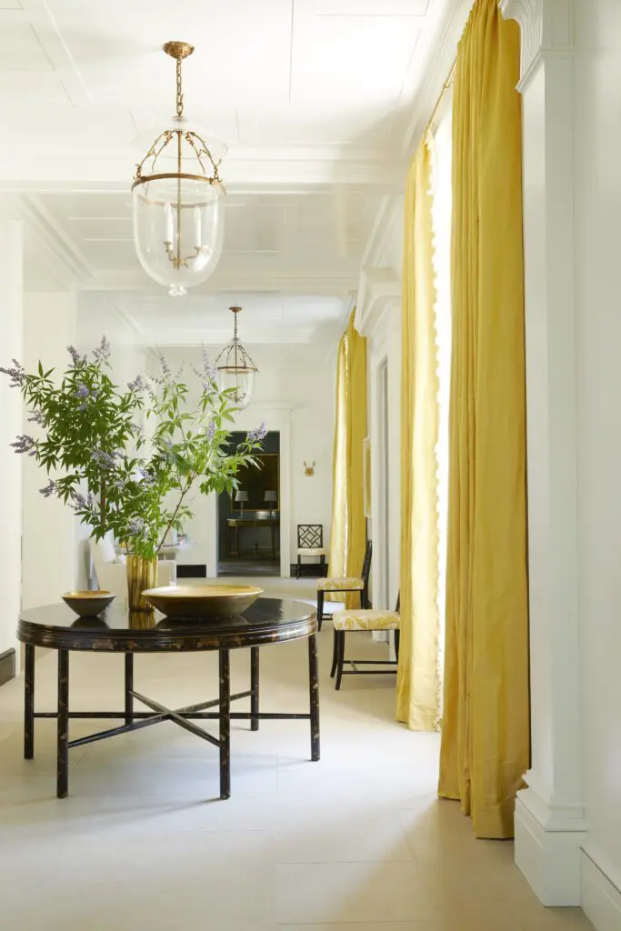 White walls in the entry hall
direct the focus to the tall windows,
where tailored silk drapes accentuate
the eleven-foot ceiling height. Dressy
as the entry’s chinoiserie table is,
there is an overall feeling of relaxed
elegance. (Photo by Melanie Acevedo)