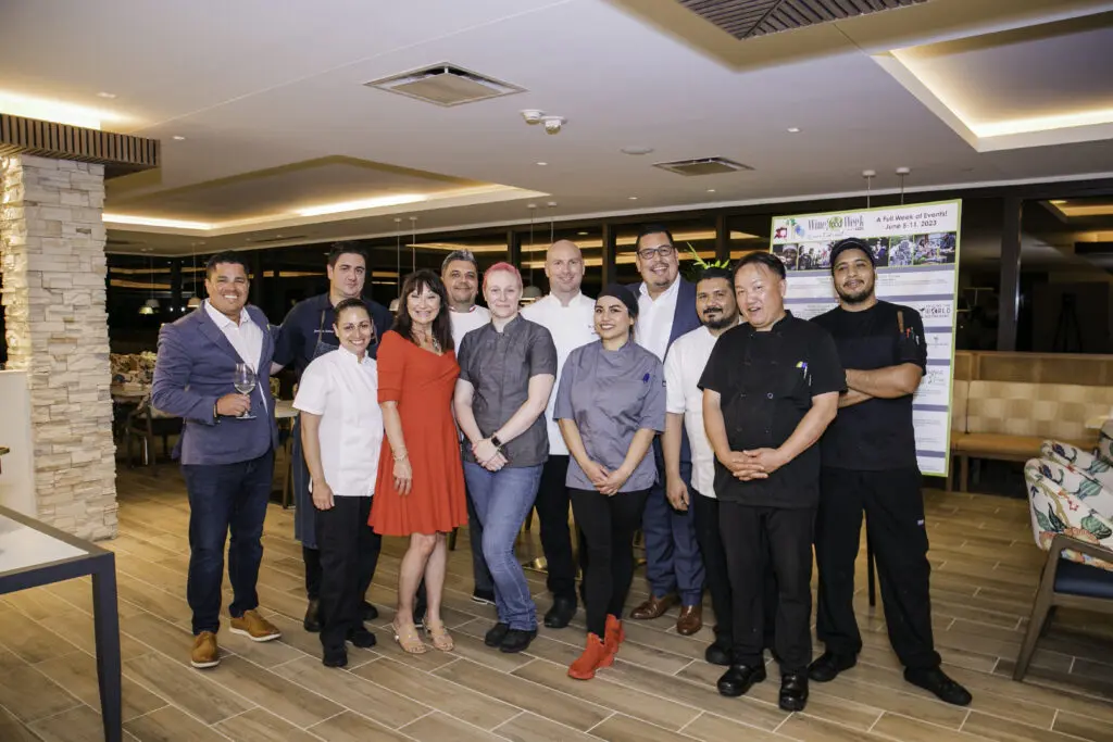 Constance McDerby in red, is surrounded by the chefs for the Wine & Food Week kickoff dinner.  Simon Solomon, far left, from Winebow. David Federico is in the back row, wearing a blue blazer. (Photo by Kelley Sweet Photography)
