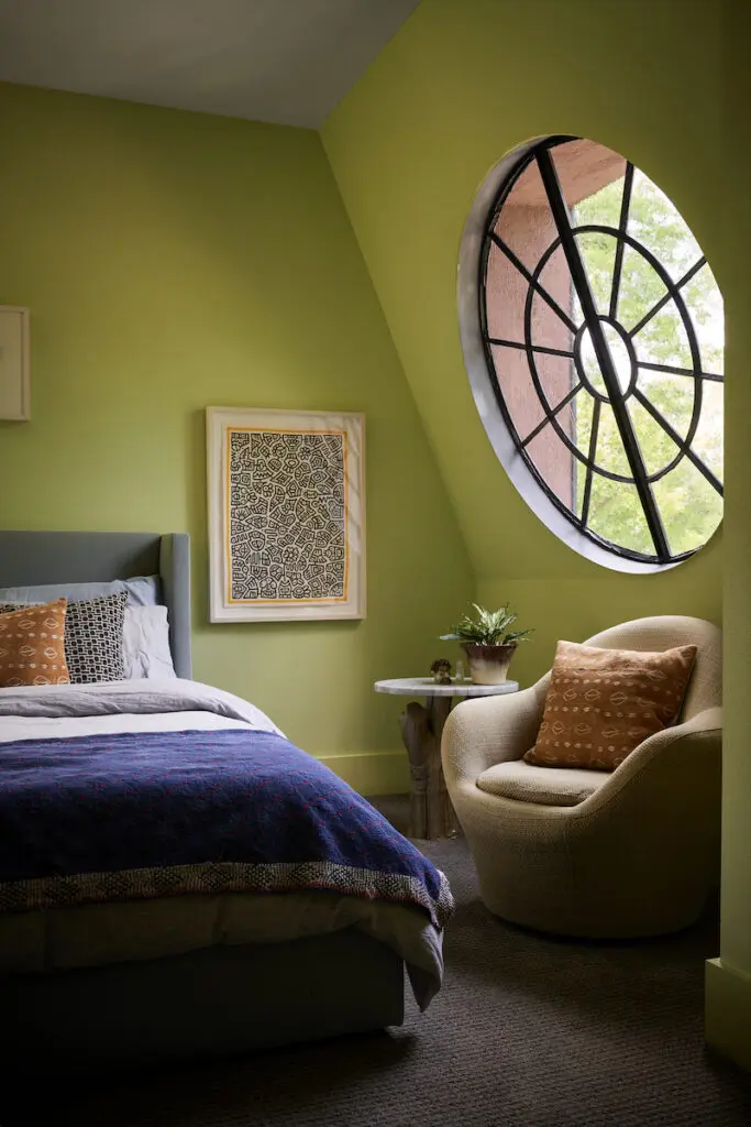 The round antique-glass window in Robert Bellamy’s bedroom slants inward like a garret apartment in Paris. Artwork by Ben Reynolds, Guatemalan coverlet from Garza Marfa. Side table made from a Japanese maple trunk.  (Photo by Pär Bengtsson)