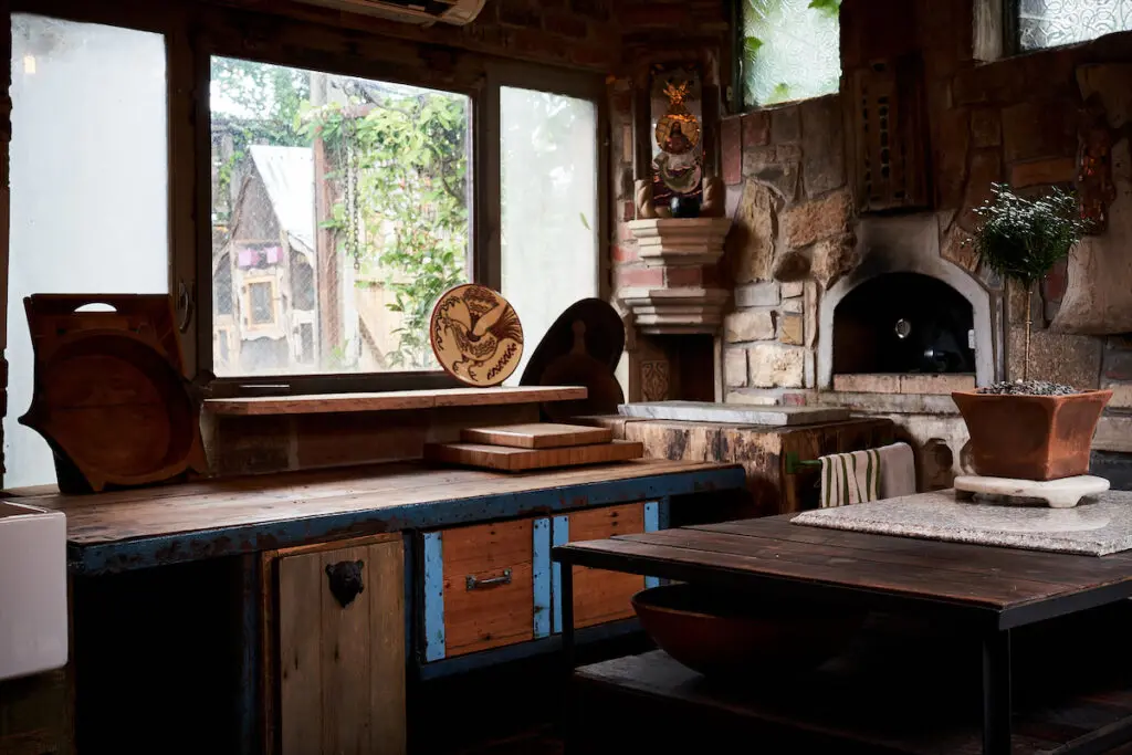 This kitchen with pizza oven was constructed from salvaged stone elements and is now enclosed. The chopping block is from a client’s former house, and the blue metal counter is repurposed from a shop on Riverfront. The salvaged window was reconfigured to prop open so he can serve guests. (Photo by Pär Bengtsson)