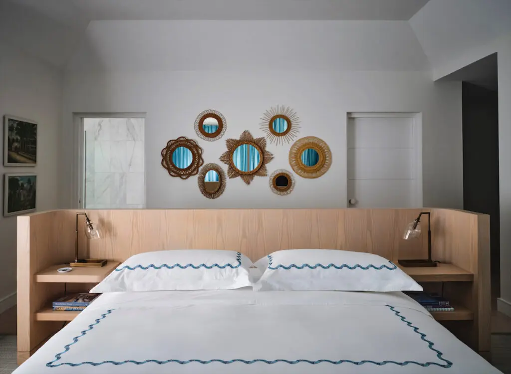 In a guest bedroom, a custom floating bed by Emily Summers Design Associates and Hamburg House linens. The collection of vintage rattan mirrors is from JF Chen, Los Angeles. (Photo by Douglas Friedman)