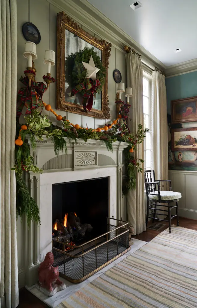 Swagged with kumquats, tangerines, and pine branches, the carved fireplace was made by Casci Ornamental Plaster and painted in Farrow & Ball French Gray. Elizabeth Eakins Studio rug. (Photo by Pär Bengtsson)