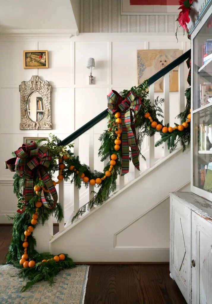 A staircase in the foyer of Cathy Kincaid’s cottage is draped with old-fashioned garlands of pine branches, mini tangerines, and kumquats handmade by Margaret Ryder of Kane & Co. (Photo by Pär Bengtsson)