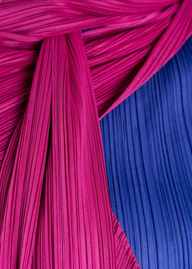 Close up of Issey Miyake's blue polyester pleated turtleneck top, Fall 1992, with pink polyester pleated coat and scarf, Fall 2004 (Photo by Shane Quereshi)