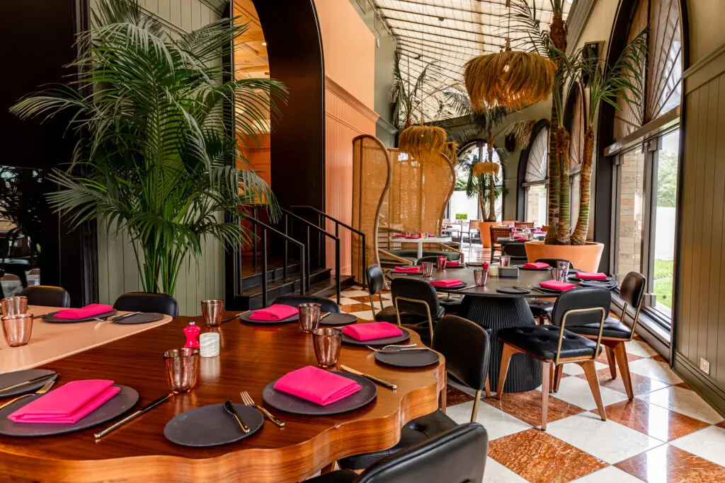 Designed by Schoos Design, the space features palm trees, magenta sofas, and original artwork by Thomas Schoos. (Photo by Samantha Marie Photography)