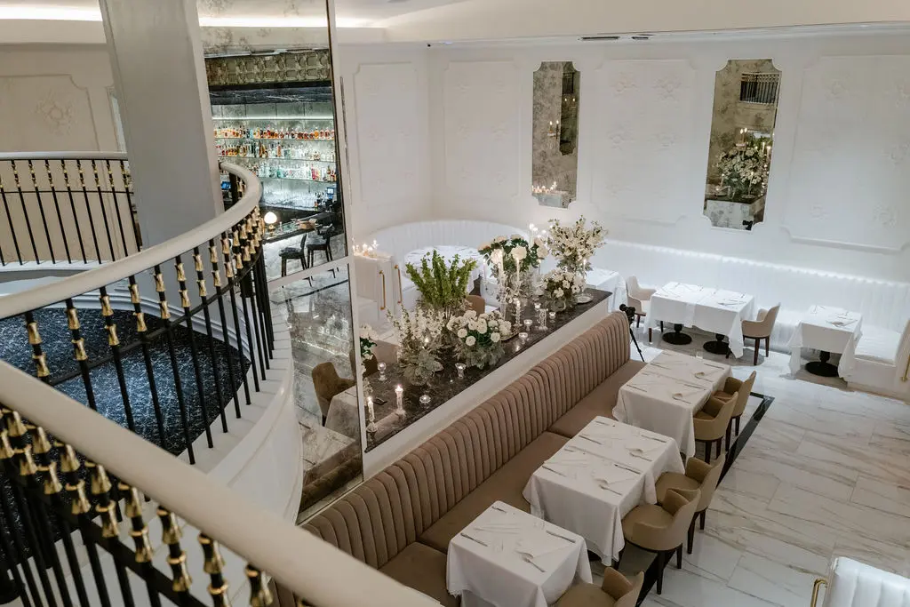 Inside the main dining room, white plaster-adorned walls and pearlized white leather channeled banquettes are punctuated with rich, dark hues. The room, expansive in both height and length, is magnified further by antiqued mirrors, while upstairs, dinner is served to the accompaniment of a baby grand piano. (Photo by Brian Kennedy)
