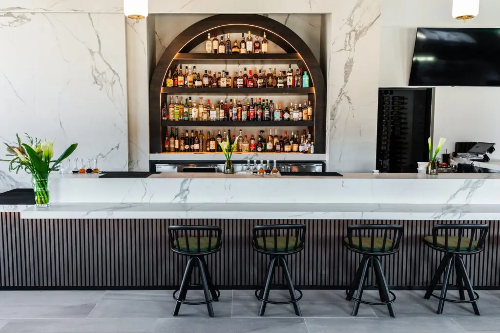 The expansive bar at the new Maven at Sawyer Yards is equipped with a sliding faux marble panel that by day when the morning rush for coffee commences can conceal the wall of spirits. (Photo by Becca Wright)