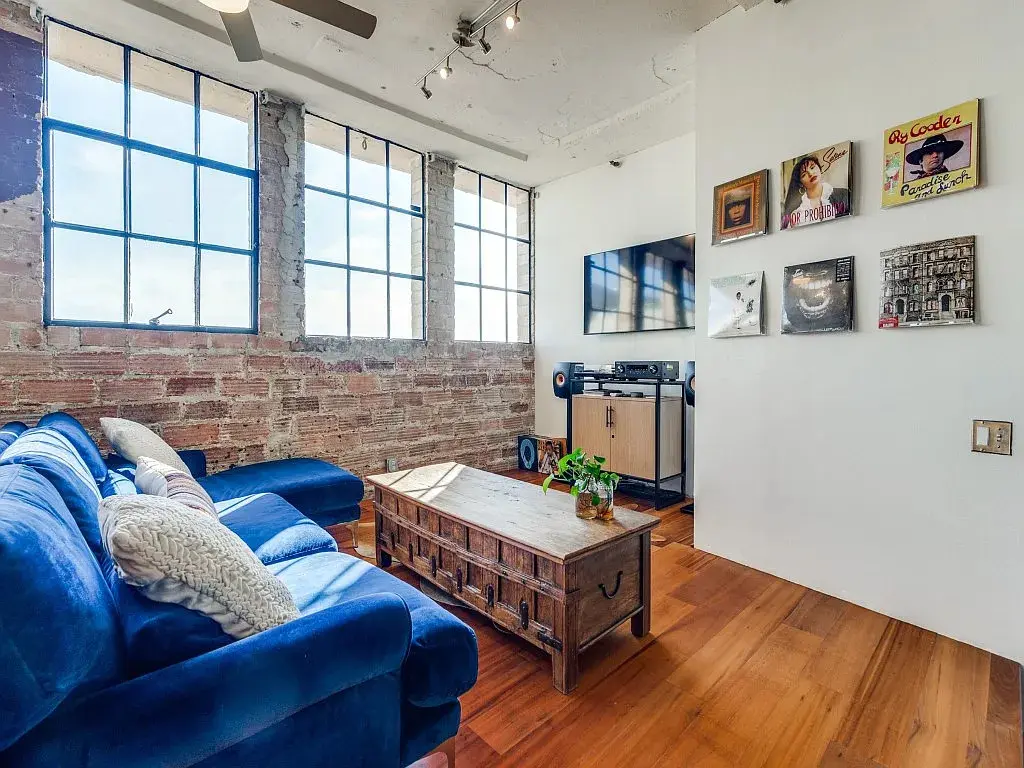 Two wooden steps lead from the kitchen to the living room, in front of an exposed brick wall.