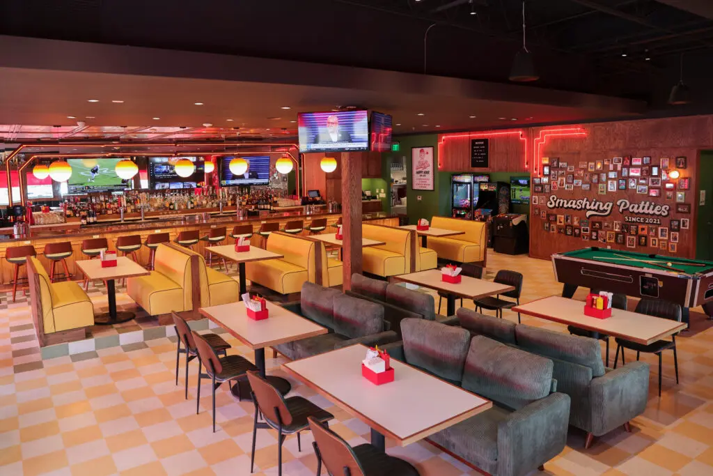 The space features bright yellow booths, neon red lights, checkered tile floors, a pool table, and an overall retro vibe. (Photo by Shafkat Anowar)