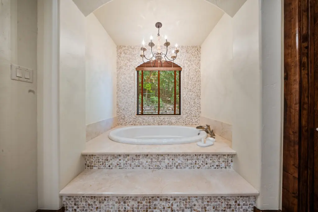 The primary suite’s spa-inspired bathroom features a soaking tub, mosaic tile, and views of the surrounding greenery. (Photo by The Ashton Agency)
