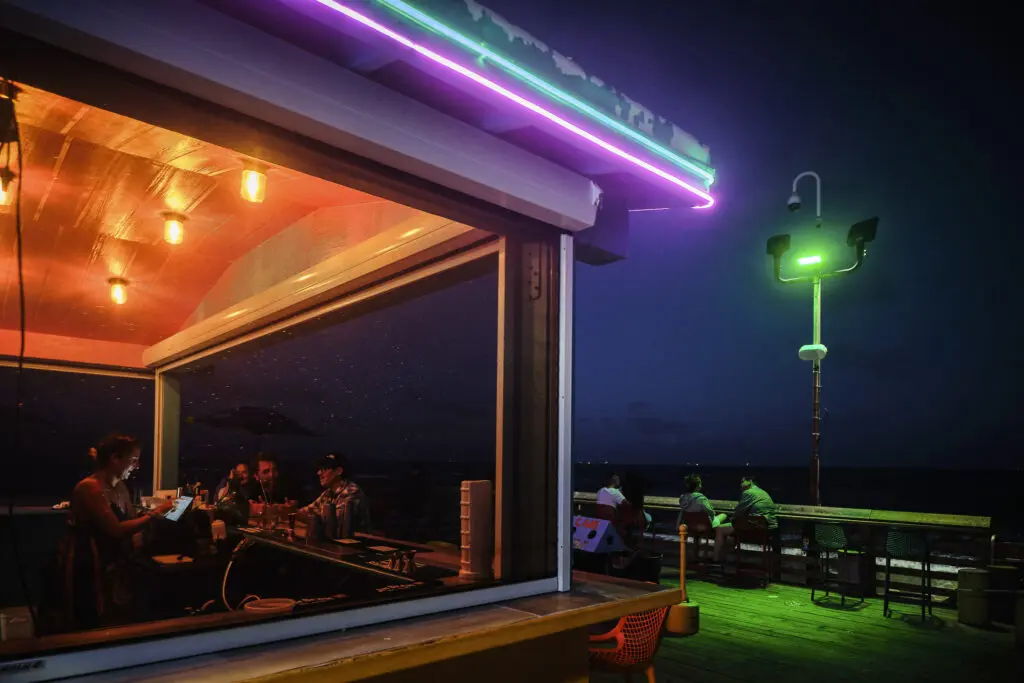 Carlos Escalona captured the glow of a neon lit café at night, where people gather inside and along the pier. (Photo courtesy Houston Center for Photography)