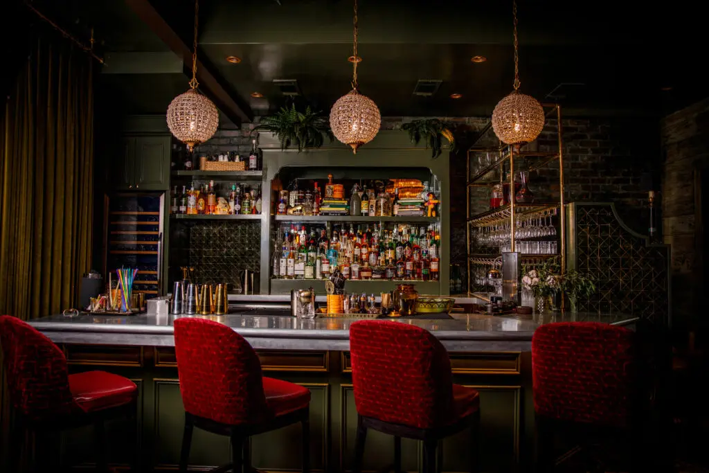 The interior of Caché uses deep greens, brass accents, and some pops of red to evoke a romantic New Orleans vibe. (Photo by Samantha Marie Photography)