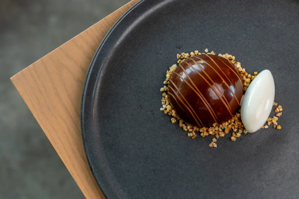 Miso butterscotch bombe is a silken whipped butterscotch mousse with a hint of miso, served under a dome-like chocolate disk drenched in dark chocolate ganache; by its side is a quenelle of pure white buckwheat gelato, the result of a laborious three-day cold-infusion process. Photo by Carla Gomez.