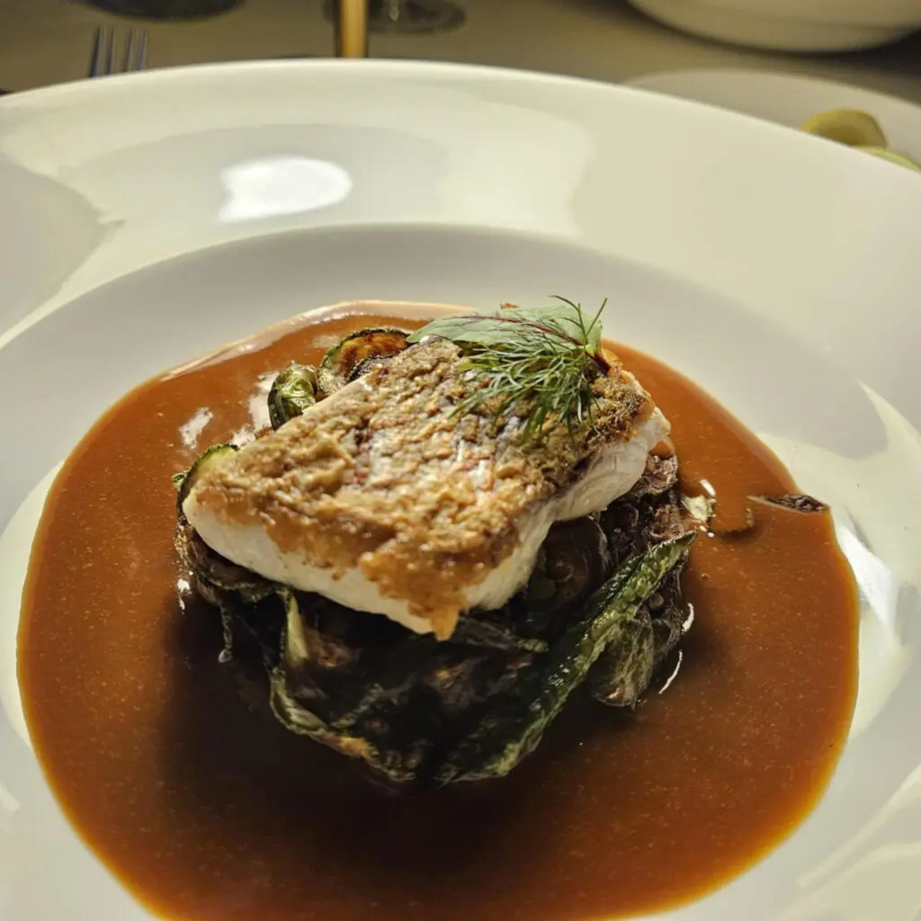 The Gulf Catch at The Crescent Hotel’s Blue Room featured a fork-tender cut of Gulf red snapper over J&BF Farms squash and charred vegetables in a savory ham-tomato broth. (Photo by Edward Brown)
