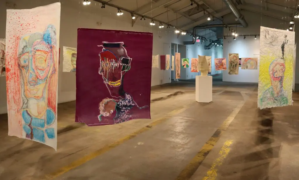 Justin Earl Grant subverts the traditional art installation by having his colorful portraits of distorted face hung and hovering around the viewer. 