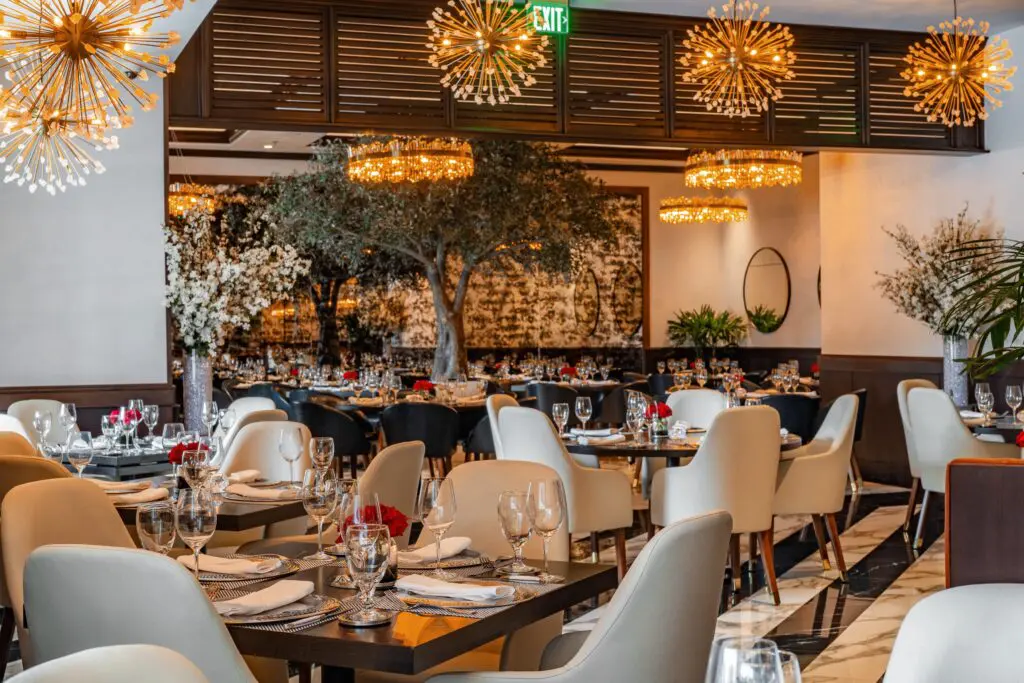 In the newly opened Truluck’s olive trees “grow” from floor to ceiling, their limbs forming a canopy over seats poised beneath in the main dining room, while the black and white tile flooring underfoot plays up the 88 keys on a baby grand. (Photo by Photos courtesy of Truluck's)