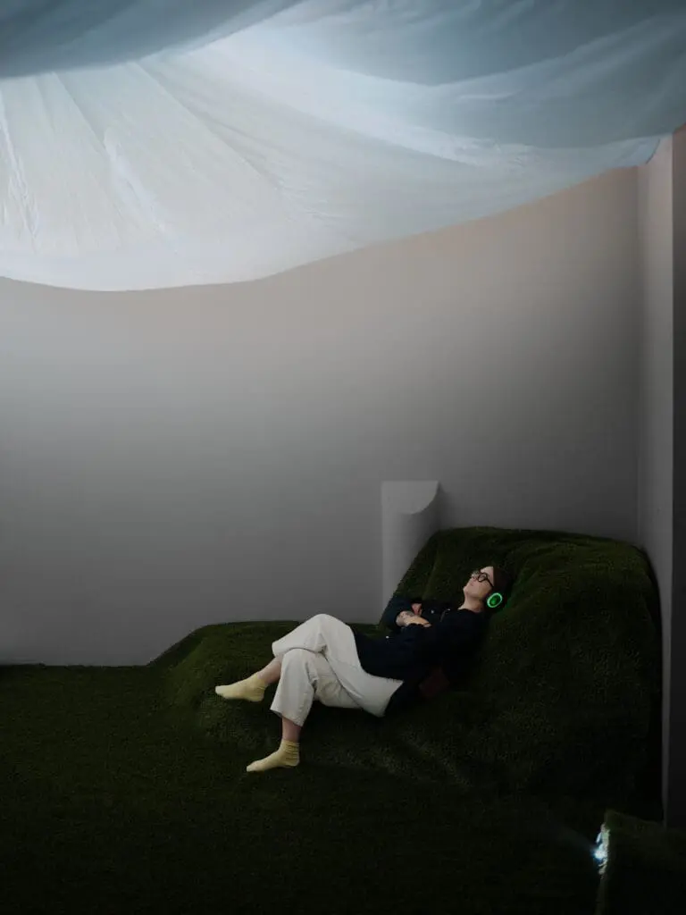 Touch Grass encourages visitors to put their phones away, remove their shoes, lie back, and ground themselves in the space while observing the projection of the sky that washes across the ceiling.  (Photo by SWOON, the studio)