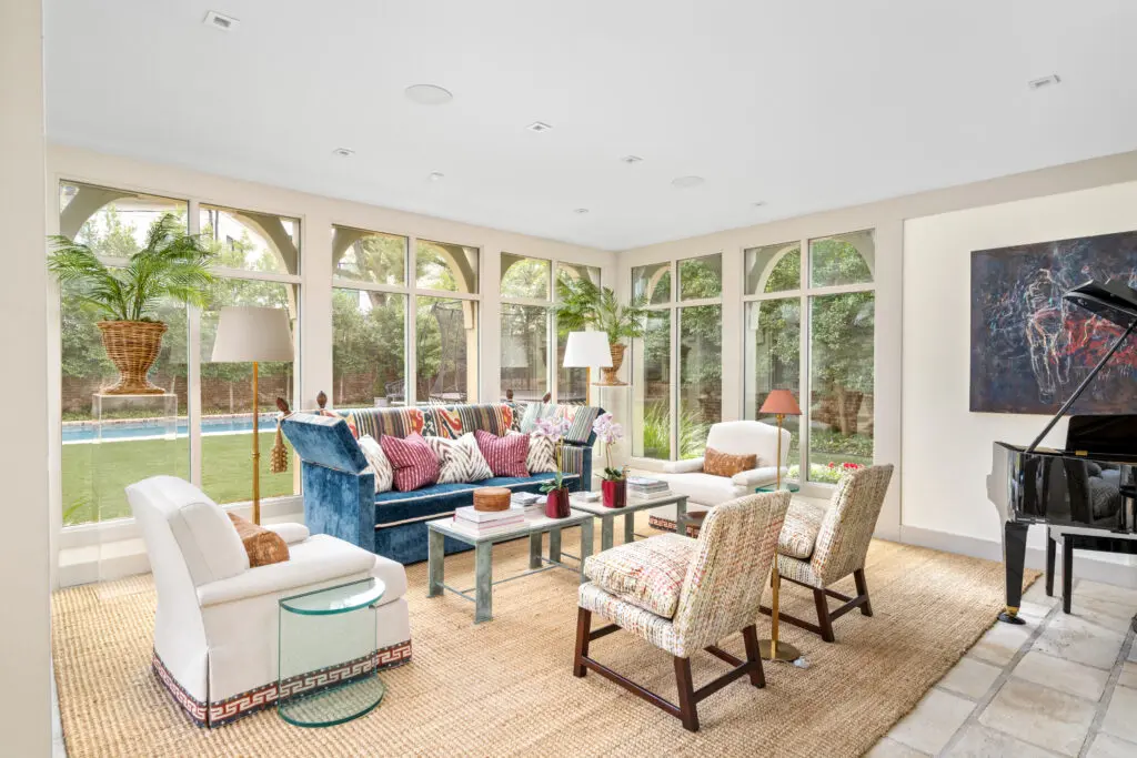 Light-filled sunroom framed by expansive windows, offering views to the terrace and pool beyond (Photo by Sonya Bertolino / Compass)