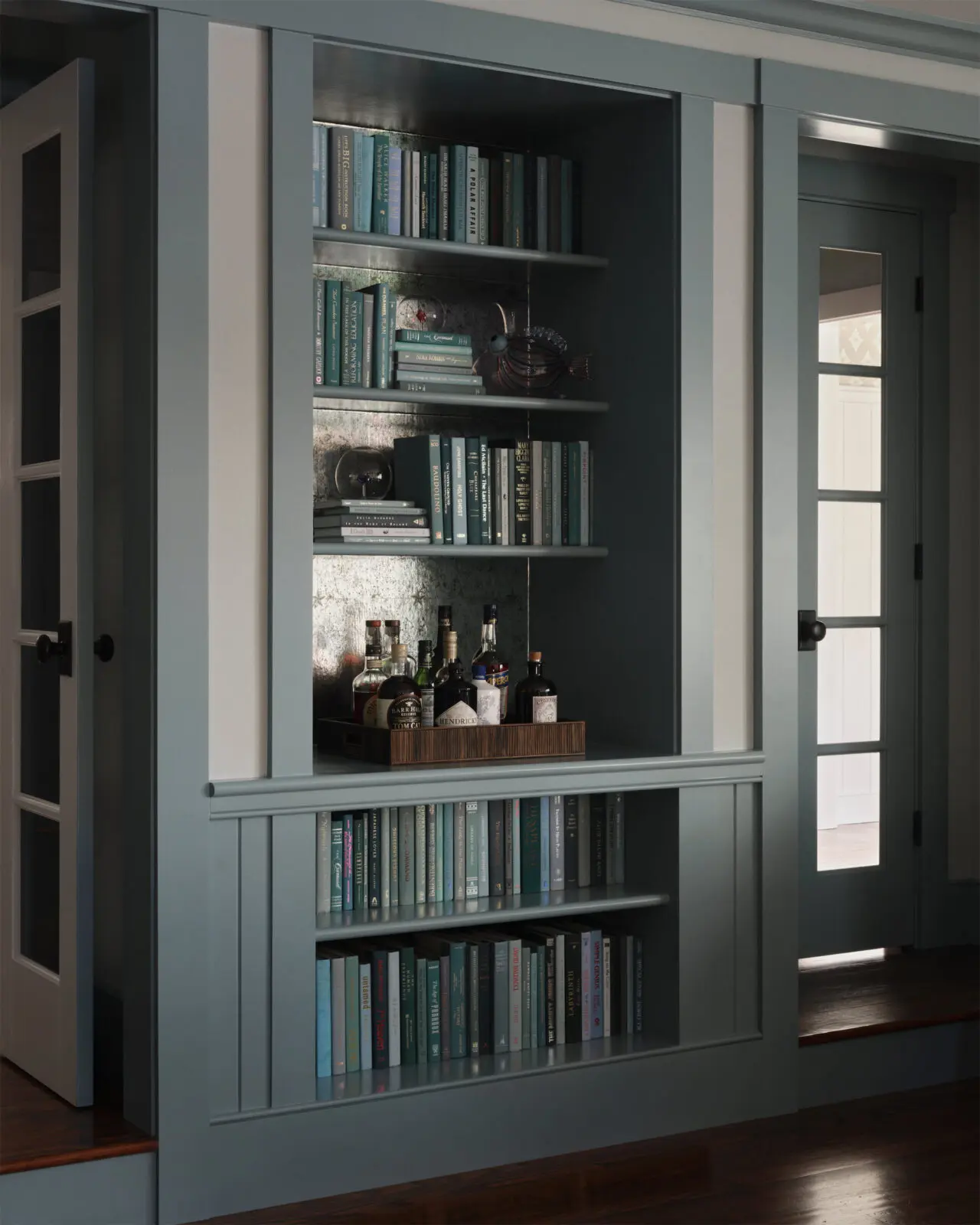 A dry bar tucked into a bookcase, with Miles Redd wallpaper from Schumacher. Dior glassware. (Photo by Douglas Friedman)