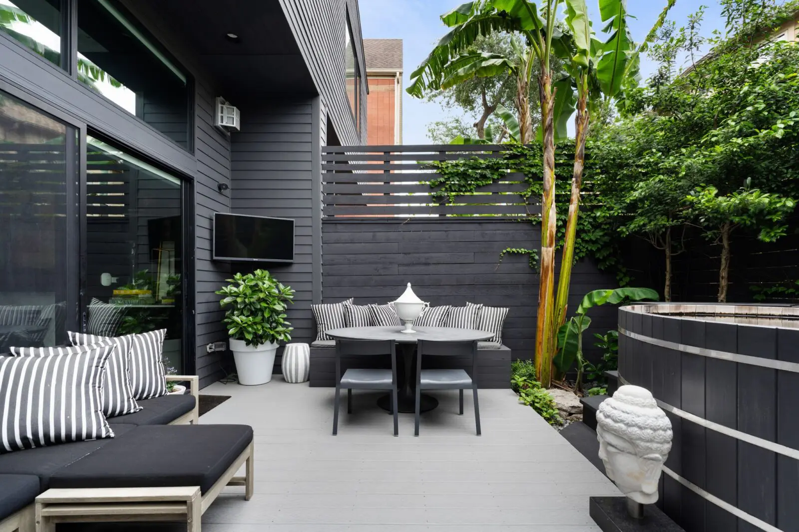 Sliding doors open to an outdoor setting with multiple seating areas, a gas grill, and lush landscaping. (Photo by Aria Media)