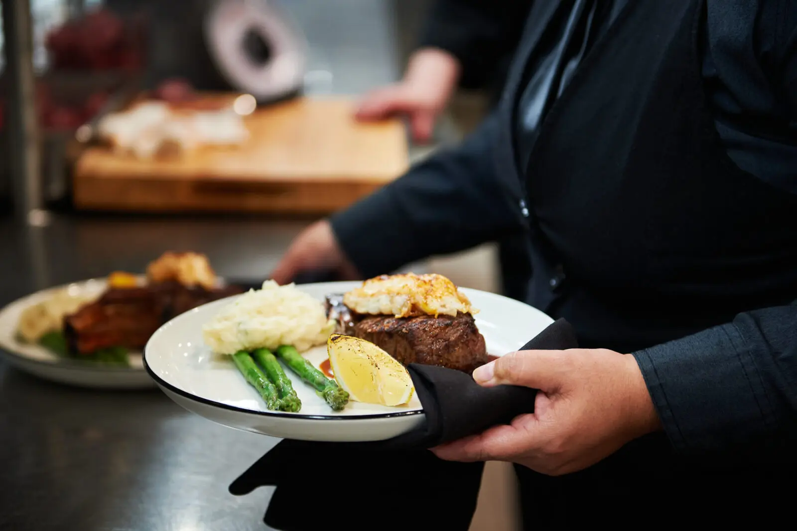 Menu highlights include an Asian Caesar salad, lamb lollipops, scallops al ajillo, miso-glazed sea bass, duck à l’orange, wagyu strip, tomahawk ribeye, and apricot bread pudding.