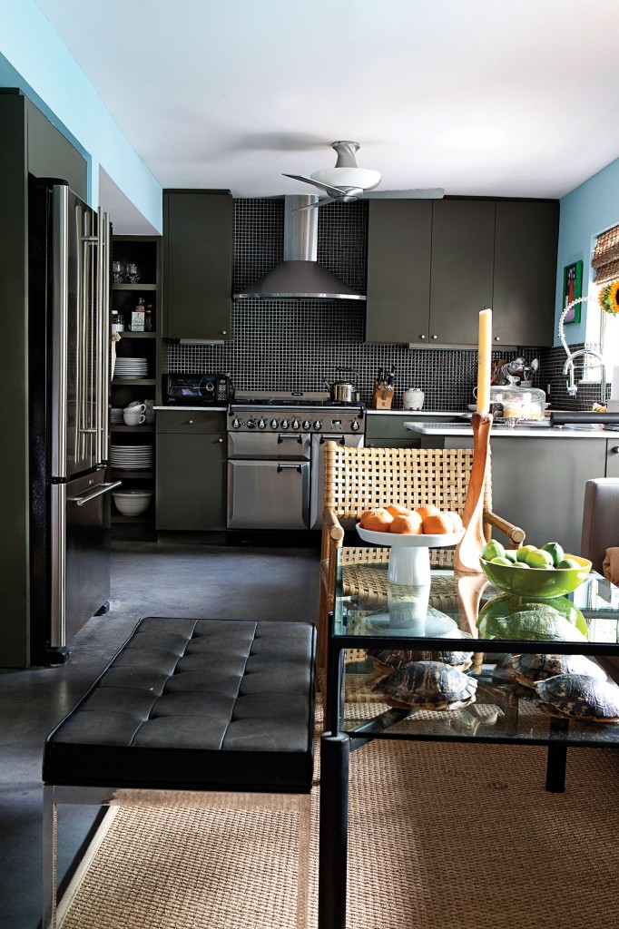 In the foreground of the kitchen, a steel-and-glass cocktail table, flanked by a Mies van der Rohe bench and McGuire seating, serves as a breakfast table. In the kitchen are honed Carrera marble countertops and a stainless AGA range.
