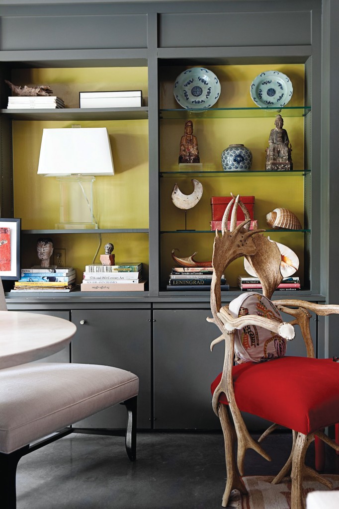 In the living room, a pair of bookshelves with lemon-lime interiors are filled with blue-and-white porcelain from Honey Church in Hong Kong, collected oddments and a glass column lamp from Restoration Hardware. Horn chair from J. Randall Powers is covered in Chinese red silk mohair from George Cameron Nash.
