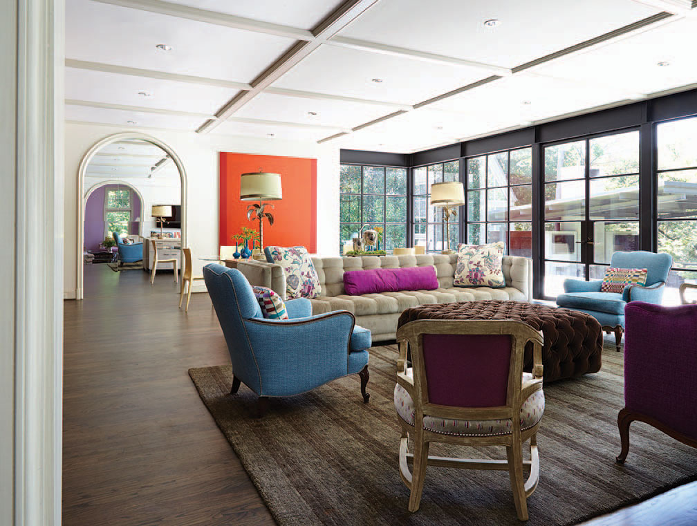 In the family room, Paul Garzotto designed the 10-foot custom sofa, which is upholstered in the same Holly Hunt indoor/outdoor velvet that covers the walls of the dining room. Sofa and tufted ottoman by Caperton Collection, through Culp Associates. The chairs are inherited pieces from both sides of the family and were re-covered by Marroquin Custom Upholstery in fabrics by Manuel Canovas and Colefax & Fowler. Damien Hirst painting.