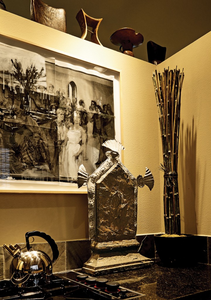 In the kitchen, a working drawing for James Drake’s City of Tells, through Moody Gallery. Above, vintage African headrests. On counter: Michael Tracy’s Iconito Para Mexico – Heart, 1985 –19886, composed of latex paint with tin corona.