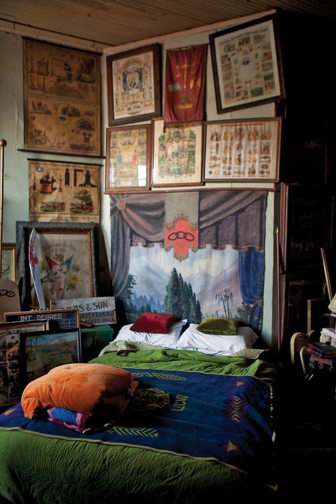 Would you sleep here? Lodge collection room with guest bed surrounded by wall of secret society paintings and lithographs.