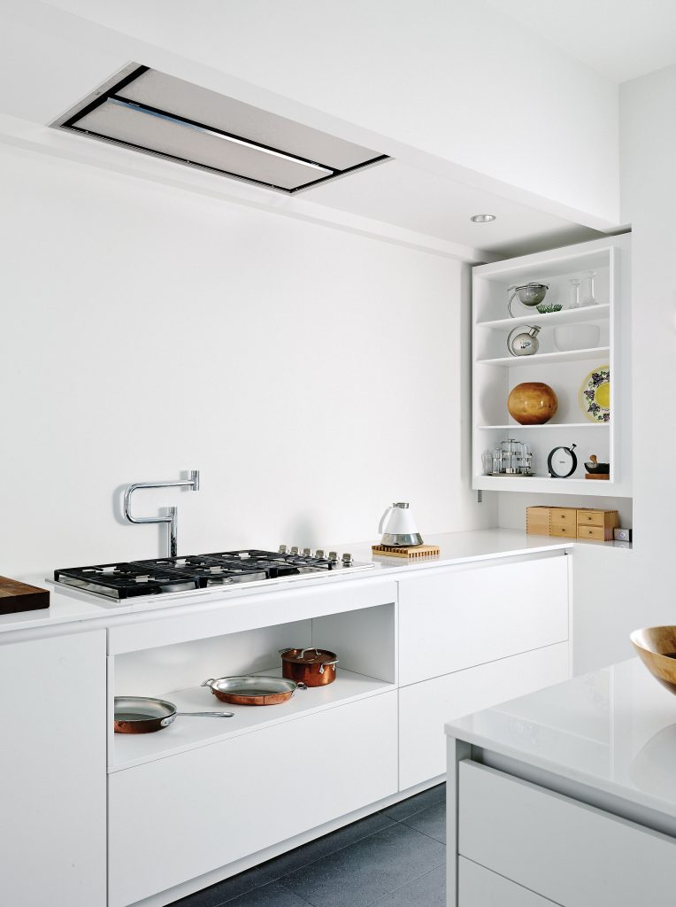 In the kitchen are Poggenpohl cabinets, custom white opaque glass countertops, Dornbracht plumbing fixtures. On the shelves, a collection of unique objects including a hand-turned wood vessel by Phillip Moulthrop and an Alessi Bauhaus martini shaker designed by Marianne Brandt. Tea kettle is an industrial design by Ross Lovegrove.