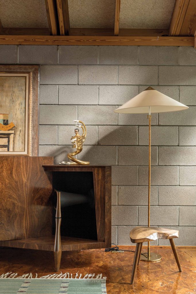 In a corner of the library, a prized 1958 JBL Paragon cabinet speaker combines the function of furniture and stereo. Resting on the Paragon is a gilded Pedro Friedeberg sculpture. Paavo Tynell Chinese Hat floor lamp and a Nakashima side table. Zemanek’s signature use of concrete blocks for the wall add an industrial edge, while maintaining elegance via the material’s direct simplicity.
