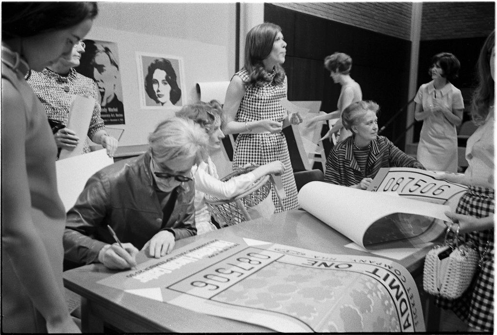 Andy Warhol signing posters, with Viva and Dominique de Menil (seated at table), University of St. Thomas, Houston, 1968. (Courtesy Menil Archives, The Menil Collection, Photo Hickey-Robertson)