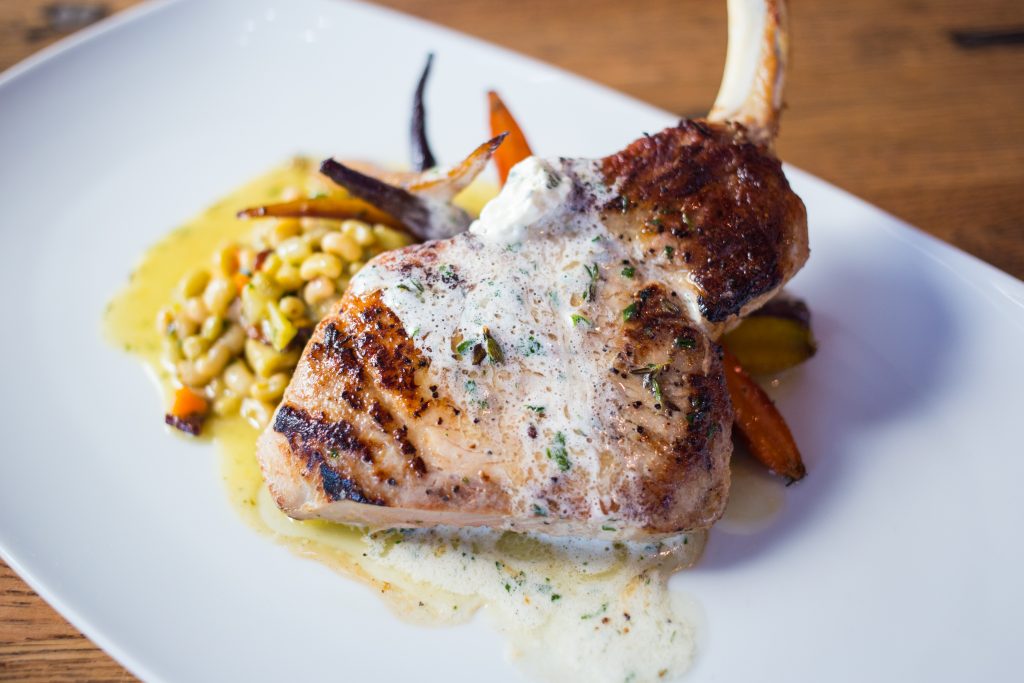 The sous vide pork chop is served with lady cream peas, glazed rainbow carrots.