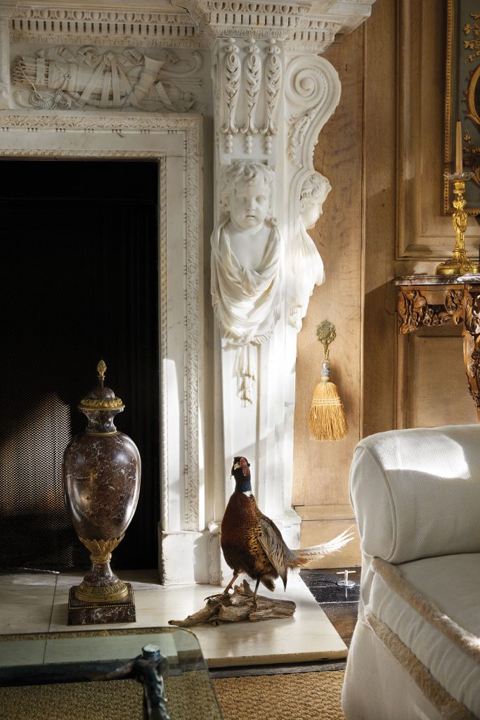 The 1729 mantel, original to Wingerworth Hall, is prized for its intricate carving and rare pure-white statuary marble. French 19th-century urn. Antique European pheasant taxidermy.