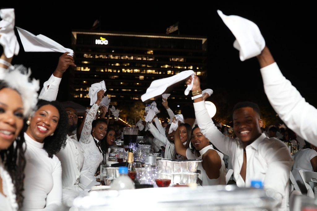 Attendees Candyce Sasu, Natalie Leonard, Tiffany Monique and Christopher King Tipps with their table groups during the traditional Dîner en Blanc napkin wave