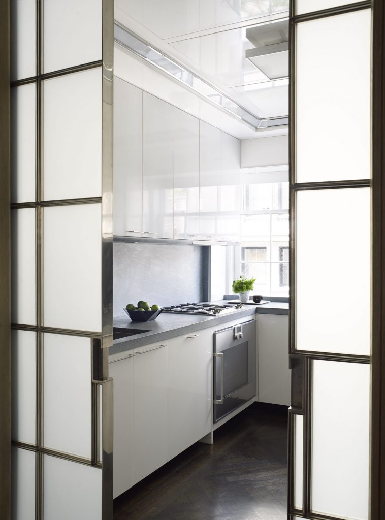 Custom doors in nickel and glass reveal a chic functional kitchen with white-lacquered cabinets and ceiling.