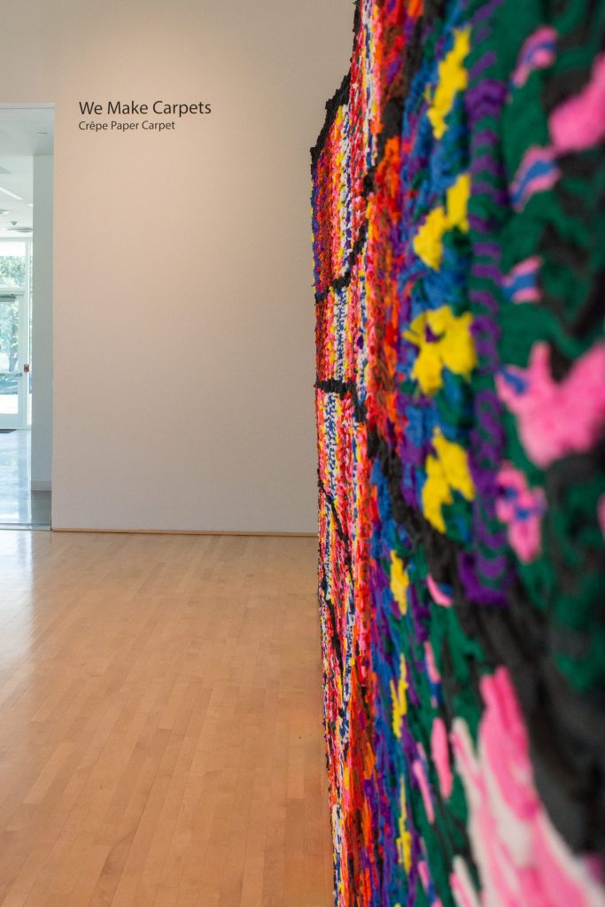 Spanning 15 feet across the room, "Crêpe Paper Carpet" by We Make Carpets is a site-specific installation made to fill the gallery space at the Moody Center with its bright colors.