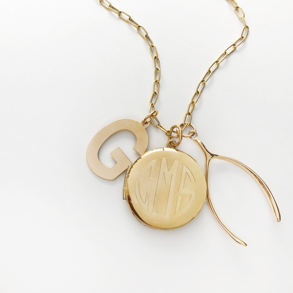 A custom necklace featuring an initial charm, engraved locket and large-scale wishbone 