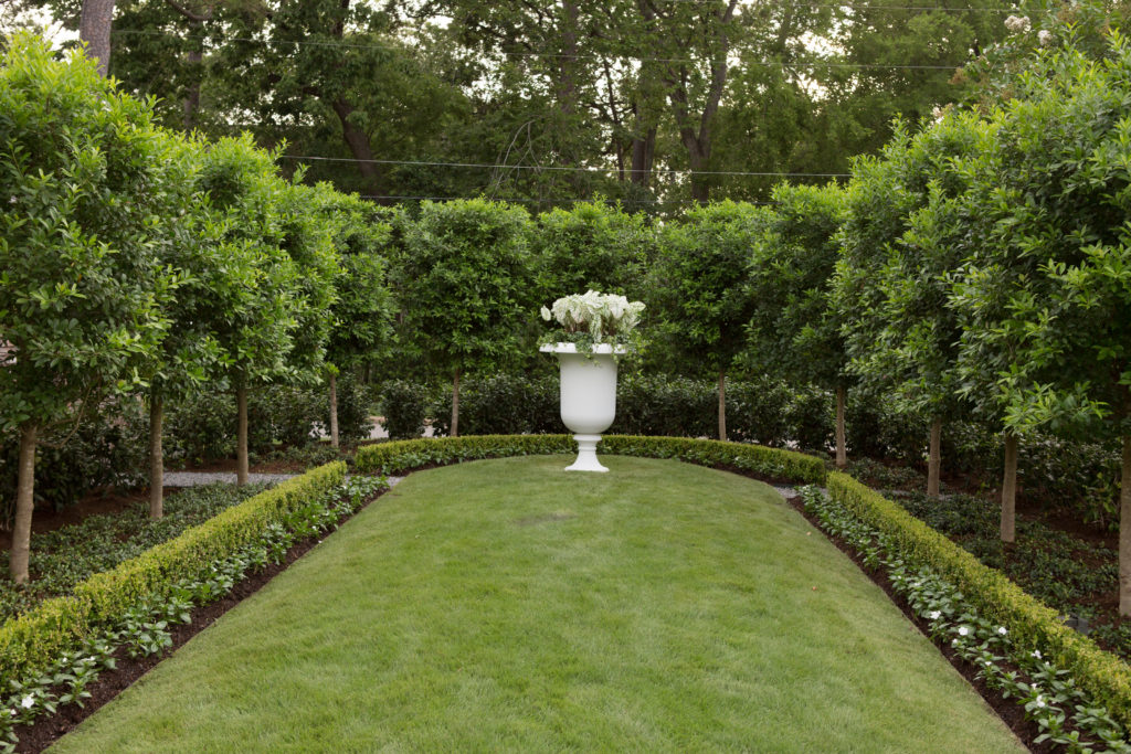  An allée of eagleston holly trees surround a white stone urn filled with white seasonal color which becomes the focal point to your left once stepping out the home (©www.kellidurham.com)