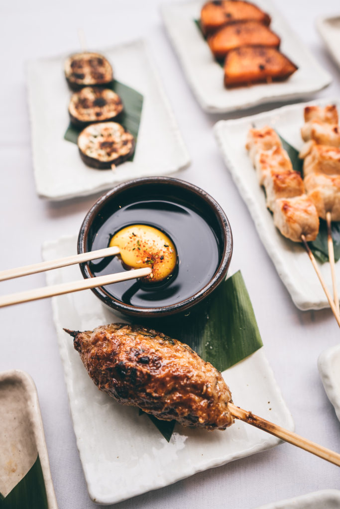 Roka Reserve's Tsukune (chicken meatball) Skewer is dipped in the egg sauce after swirling to break the yoke into the liquid.