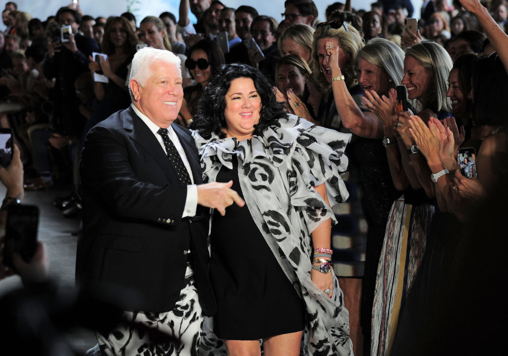 Dennis Basso and Ashley Longshore greet an adoring audience at the end of his runway show. (Photo by Owen Hoffmann/Patrick McMullan via Getty Images)