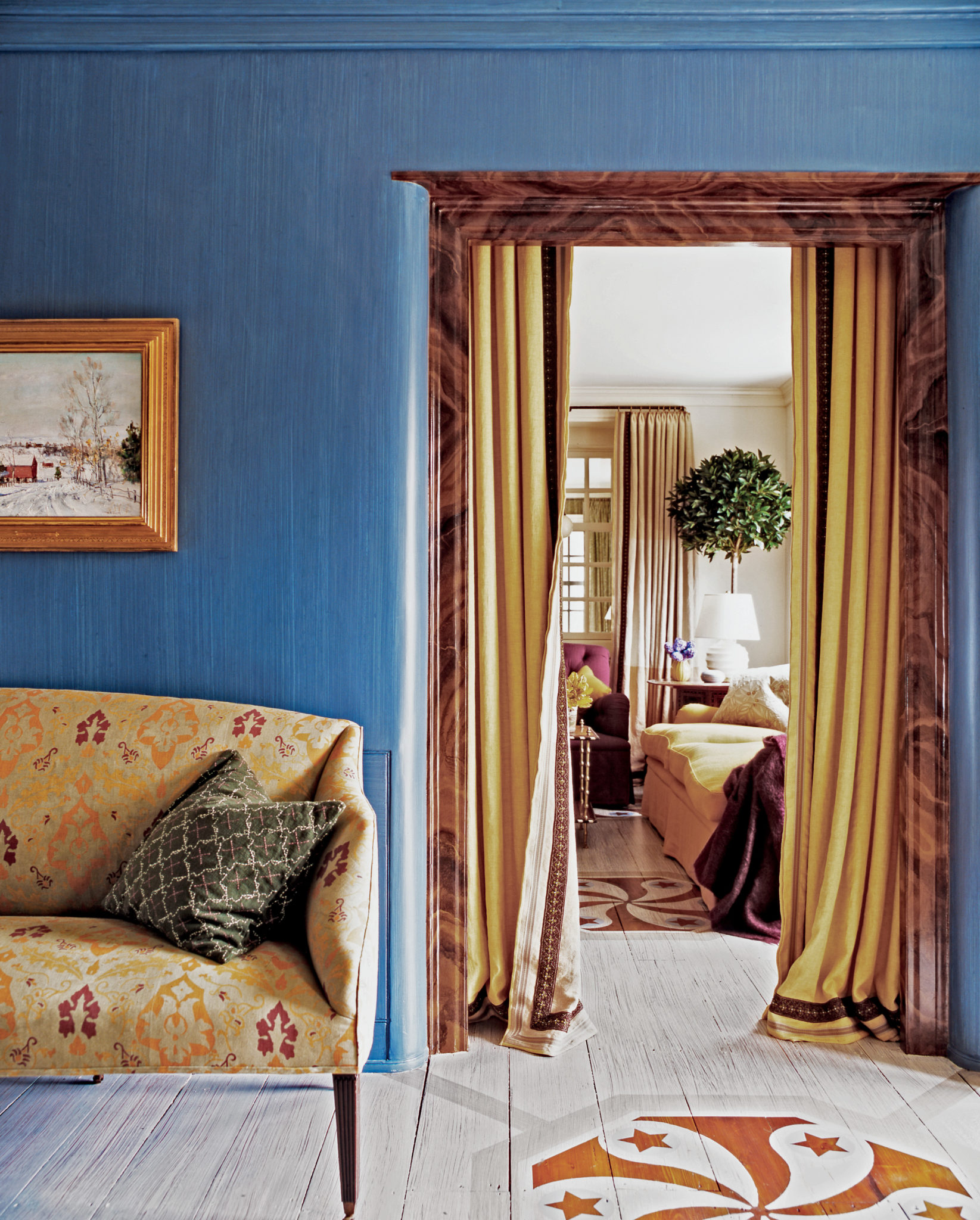 An intense blue entrance connects to a white living room through the consistency of a painted floor, while the pattern on the settee has a touch of the gourd color found in the curtains and then again on the sofa in the next room.