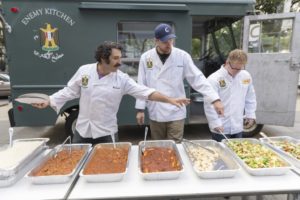 Michael Rakowitz pictured with his “Enemy Kitchen” on the Museum of Contemporary Art Chicago plaza, 2017. The food-based project taps Iraqi refugees and immigrants as chefs, and creates a dialogue when the audience comes together over a shared meal. (© MCA Chicago; photo Nathan Keay; courtesy artnet.com)