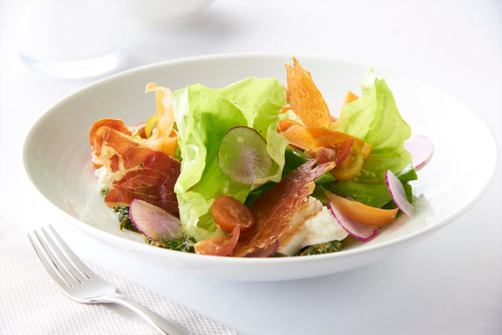 A burrata and butter lettuce salad features La Quercia Iowa prosciutto, cherry tomatoes, basil pesto, and aged balsamic.