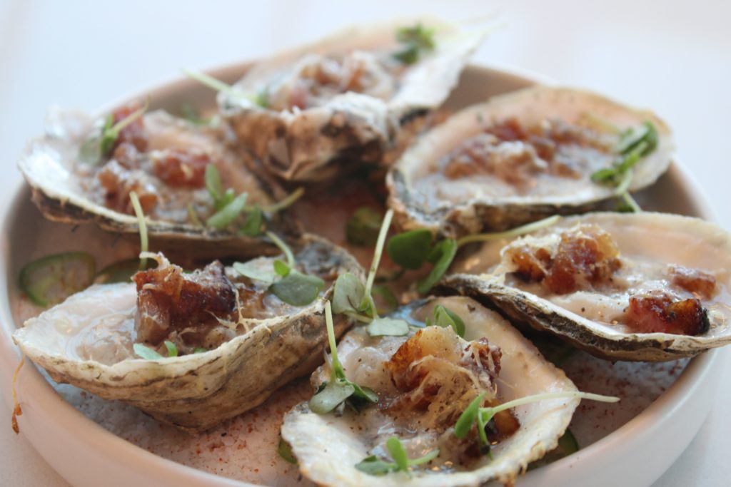 Grilled oysters served with garlic, Parmesan, and guanciale pork. Photo by Brittany Baerwald.